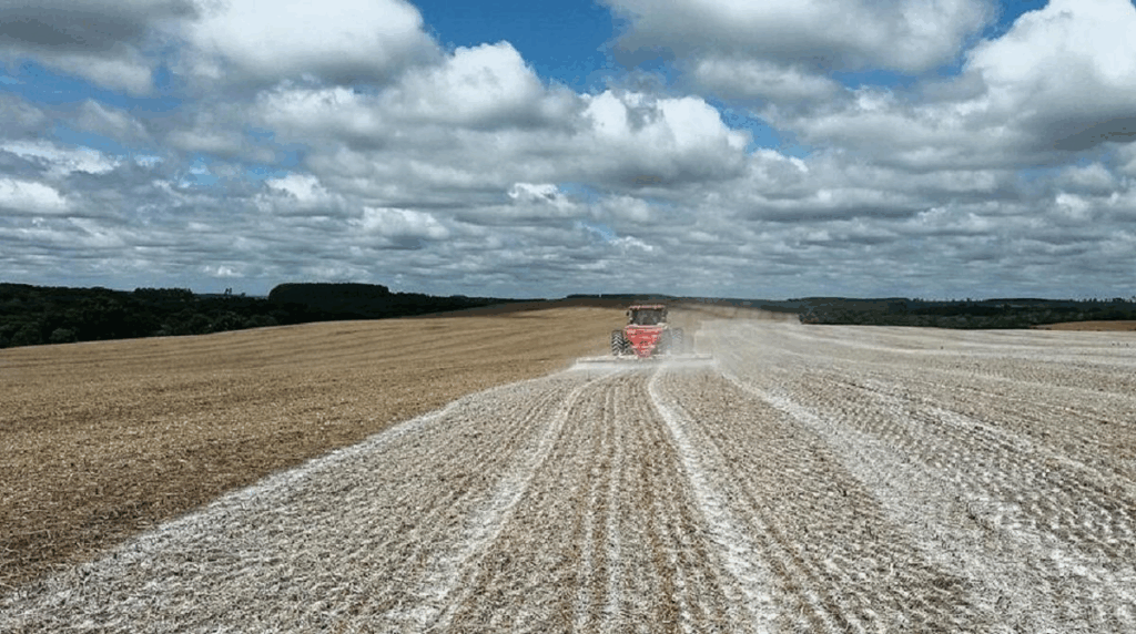 operação agrícola em larga escala, mostrando um trator vermelho aplicando um corretivo de solo, provavel