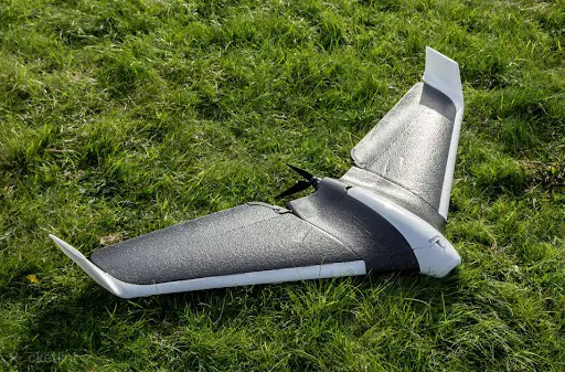 drone de asa fixa, provavelmente um modelo eBee, pousado sobre um gramado verde. O equipamento, com design