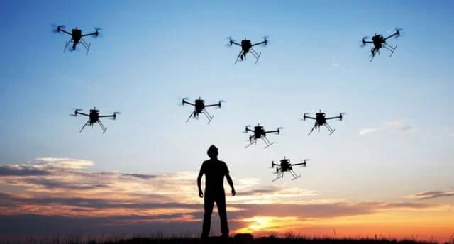 a silhueta de uma pessoa, possivelmente um agricultor ou engenheiro agrônomo, em pé num campo ao entardecer. O