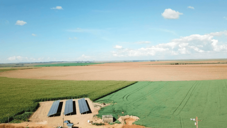 uma ampla paisagem rural sob um céu azul e ensolarado, capturada de uma perspectiva aérea. Em primeiro plano,