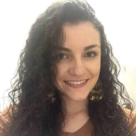 retrato em close-up de uma mulher sorridente com longos cabelos escuros e cacheados. Ela olha diretamente para
