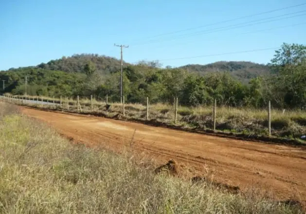 uma paisagem rural sob um céu azul e limpo. Em destaque, uma estrada de terra batida, de coloração avermelhada
