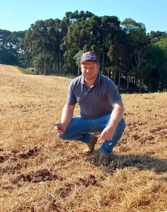 produtor rural ou agrônomo agachado em um campo agrícola após a colheita, que está coberto por palhada se