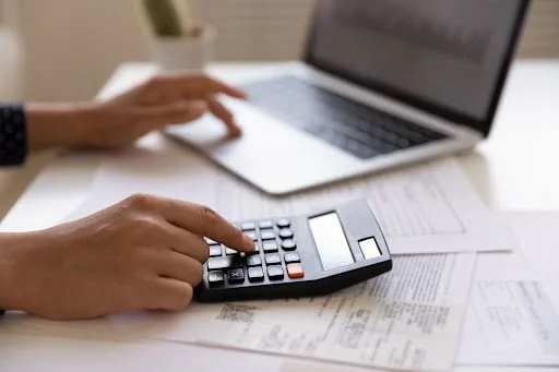 close-up das mãos de uma pessoa em uma mesa de trabalho branca, realizando tarefas de gestão financeira. U