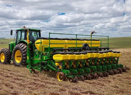 conjunto de maquinário agrícola de grande porte em plena operação no campo. Em primeiro plano, um trator ve