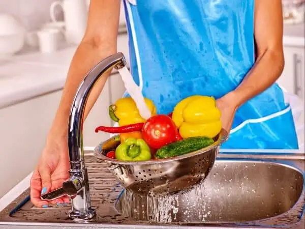 pessoa, vestindo um avental azul, em uma cozinha lavando uma variedade de vegetais frescos e coloridos. U