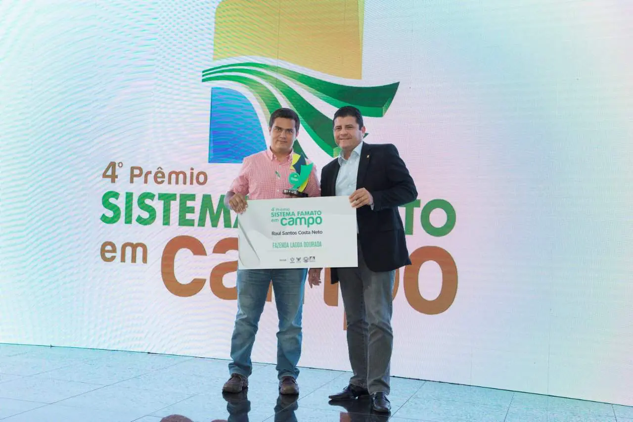 momento de premiação durante o ‘4º Prêmio Sistema FAMATO em Campo’. Dois homens estão em destaque no palc
