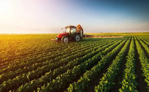 cena emblemática do agronegócio moderno: um trator vermelho, equipado com um pulverizador, percorre uma