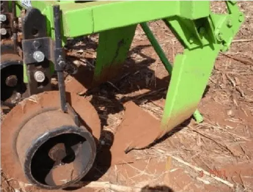 close-up detalhado de um implemento agrícola em plena operação no campo. O equipamento, com sua estrutura m