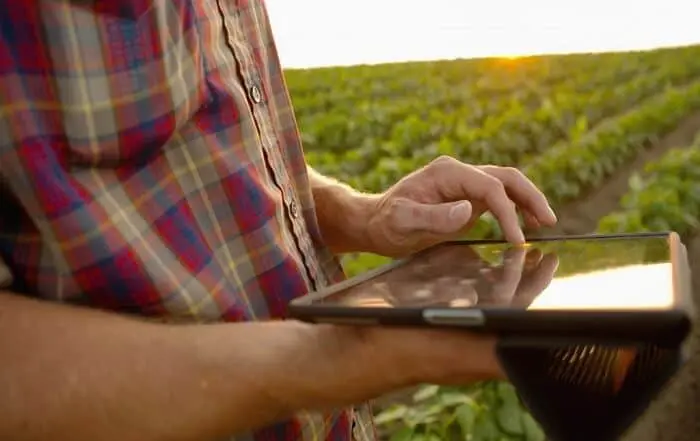 close-up de um agricultor em meio a uma lavoura, com o sol se pondo ou nascendo ao fundo, criando uma ilu