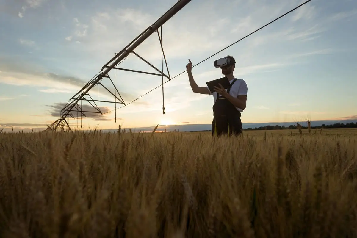 agricultor moderno ou técnico agrícola em meio a uma vasta plantação de trigo ao entardecer. Ele está uti