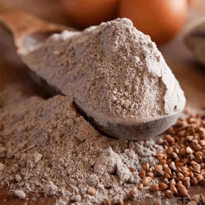 uma cena rústica e detalhada focada na farinha de trigo sarraceno. Em primeiro plano, uma colher de pau está r